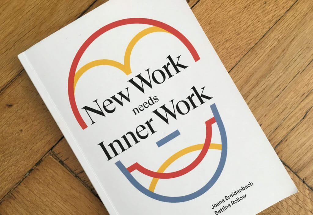 Ein Buch mit dem Titel „New Work needs Inner Work“ liegt auf einem Holzboden.