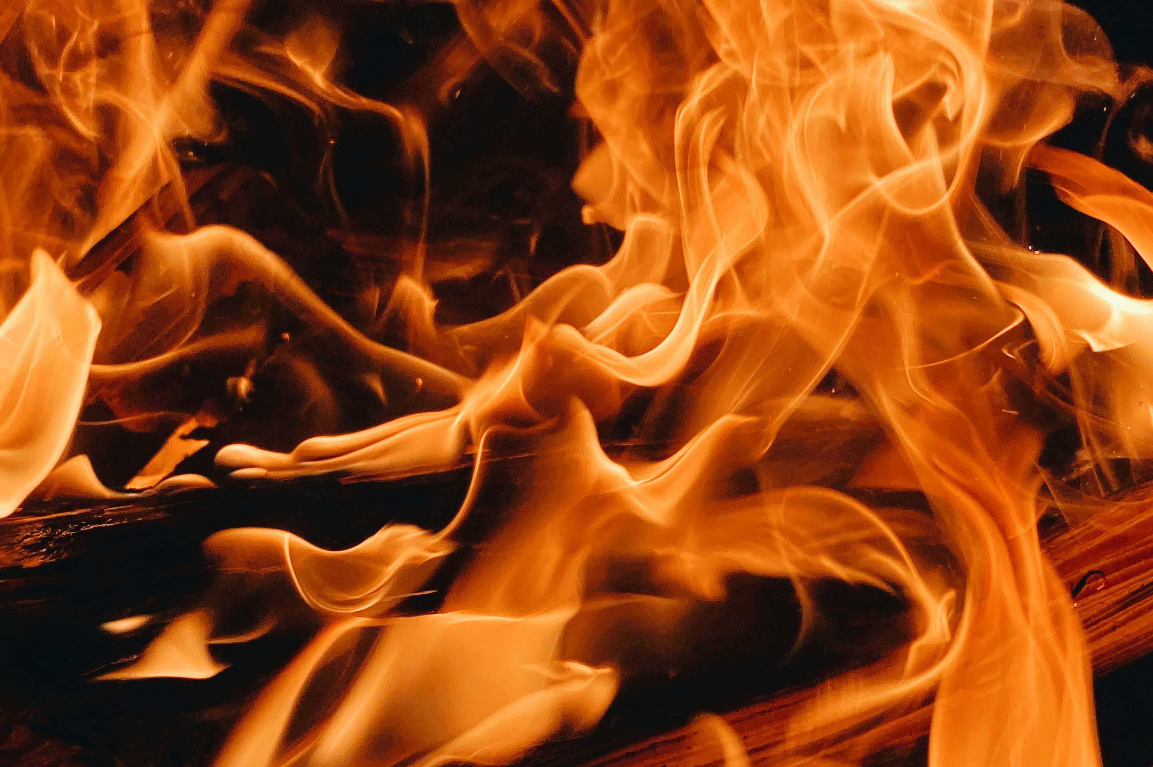 Nahaufnahme von leuchtend orangefarbenen Flammen und brennendem Holz, wobei auf dem Bild wirbelnder Rauch und intensive Hitze zu sehen sind.